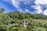 Luxurious villas with pointed roofs are nestled amidst lush tropical greenery. Dense foliage surrounds the buildings, creating a peaceful and secluded atmosphere. A bright blue sky with wispy white clouds stretches overhead.