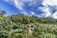 Luxurious villas with pointed roofs are nestled amidst lush tropical greenery. Dense foliage surrounds the buildings, creating a peaceful and secluded atmosphere. A bright blue sky with wispy white clouds stretches overhead.