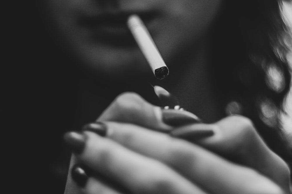 Photographie en niveaux de gris d’une femme allumant une cigarette