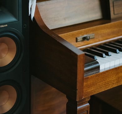 black subwoofer speaker beside brown wooden pianoa