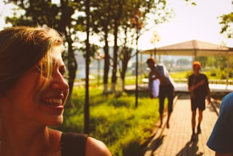 A smiling participant being helped by a support worker into a community center, with a sunny park in the background.