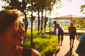 A woman smiling in a soft pastel t-shirt, surrounded by greenery in a sunny park.