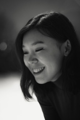 A black and white portrait of a transgender American smiling gently, framed by soft natural light.