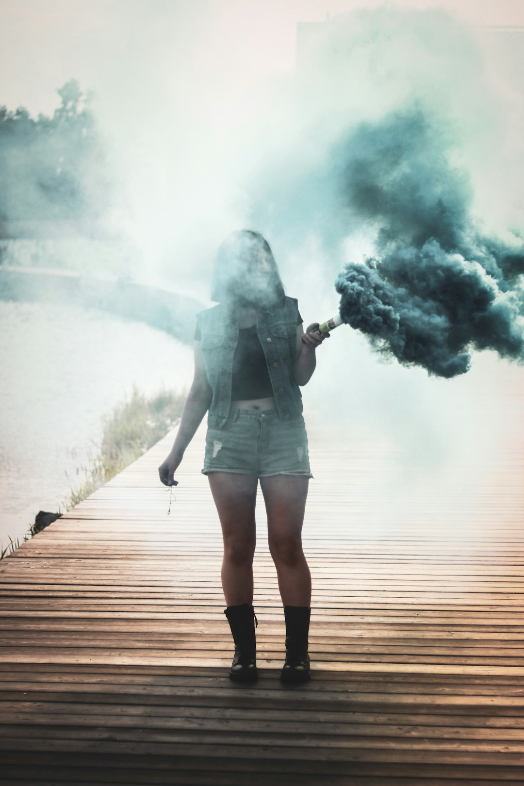 woman standing on wooden dock holding tube with smoke