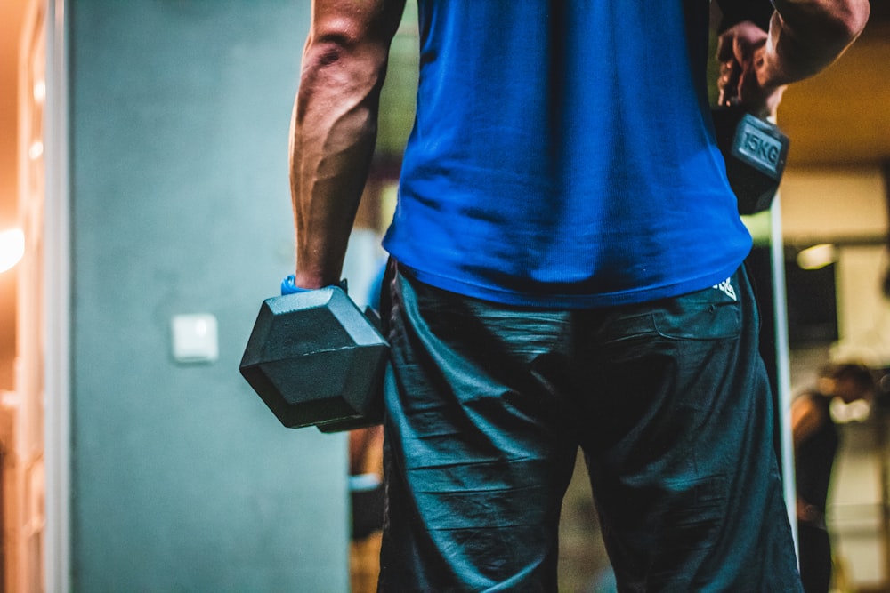 man in blue shirt carrying black dumbbells