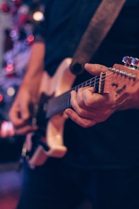 A close-up of hands playing an electric guitar with a rock band backdrop.