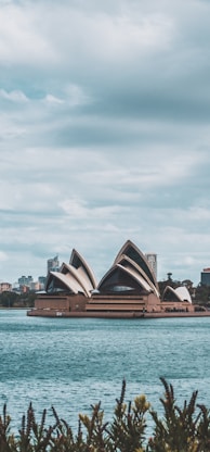 Syndey Opera House facing body of water under cloudy sky