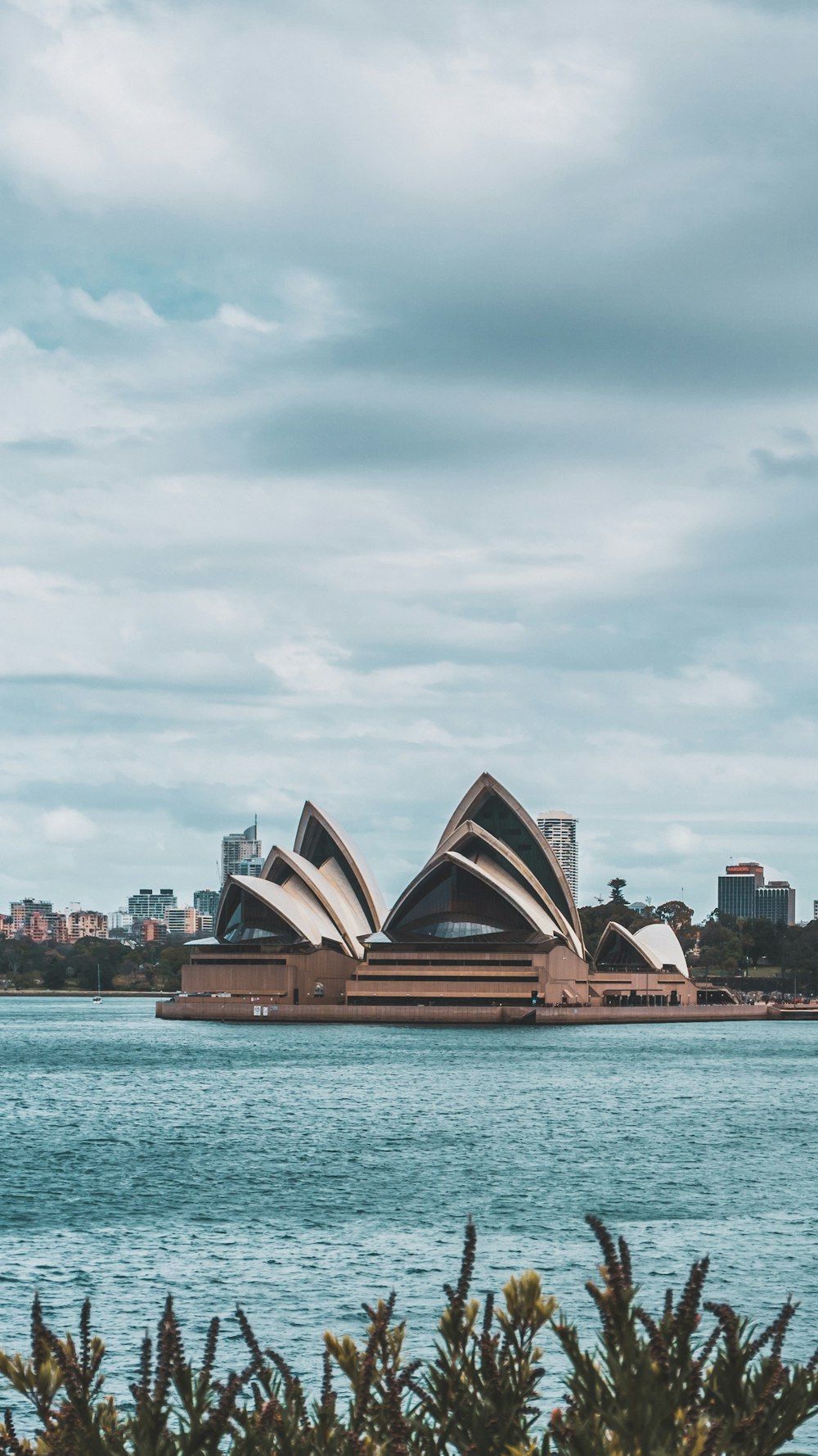 Syndey Opera House facing body of water under cloudy sky