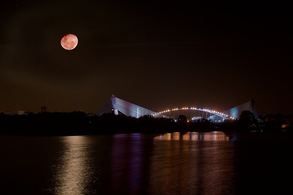 lighted arch bridge and body of water under red moon