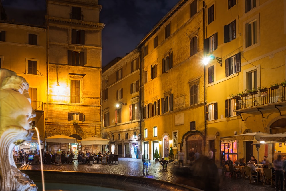 people walking and standing near brown concrete buildings during nighttime