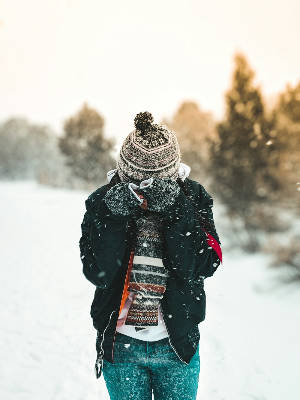 ボブルハットと黒いジップアップジャケットを着た人が雪に覆われたフィールドに立っている