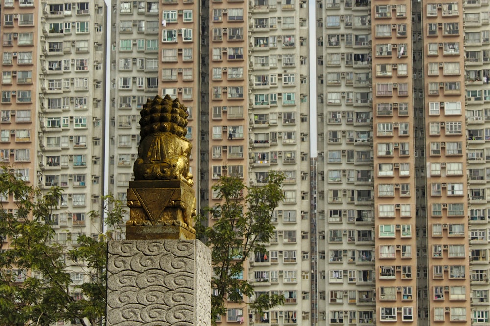 gold-colored statue facing concrete high-rise buildings during daytime