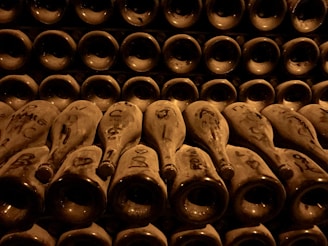 A close-up of an elegant vintage wine bottle resting on aged wooden barrels in a dimly lit cellar.