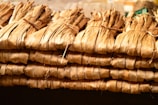 Bundles of dried leaves are tightly tied together with string, stacked in a neat, organized manner. The leaves have a brownish, natural hue and appear to be used for traditional or organic purposes.