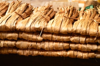 Bundles of dried leaves are tightly tied together with string, stacked in a neat, organized manner. The leaves have a brownish, natural hue and appear to be used for traditional or organic purposes.