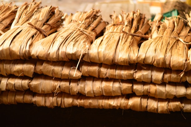 Bundles of dried leaves are tightly tied together with string, stacked in a neat, organized manner. The leaves have a brownish, natural hue and appear to be used for traditional or organic purposes.