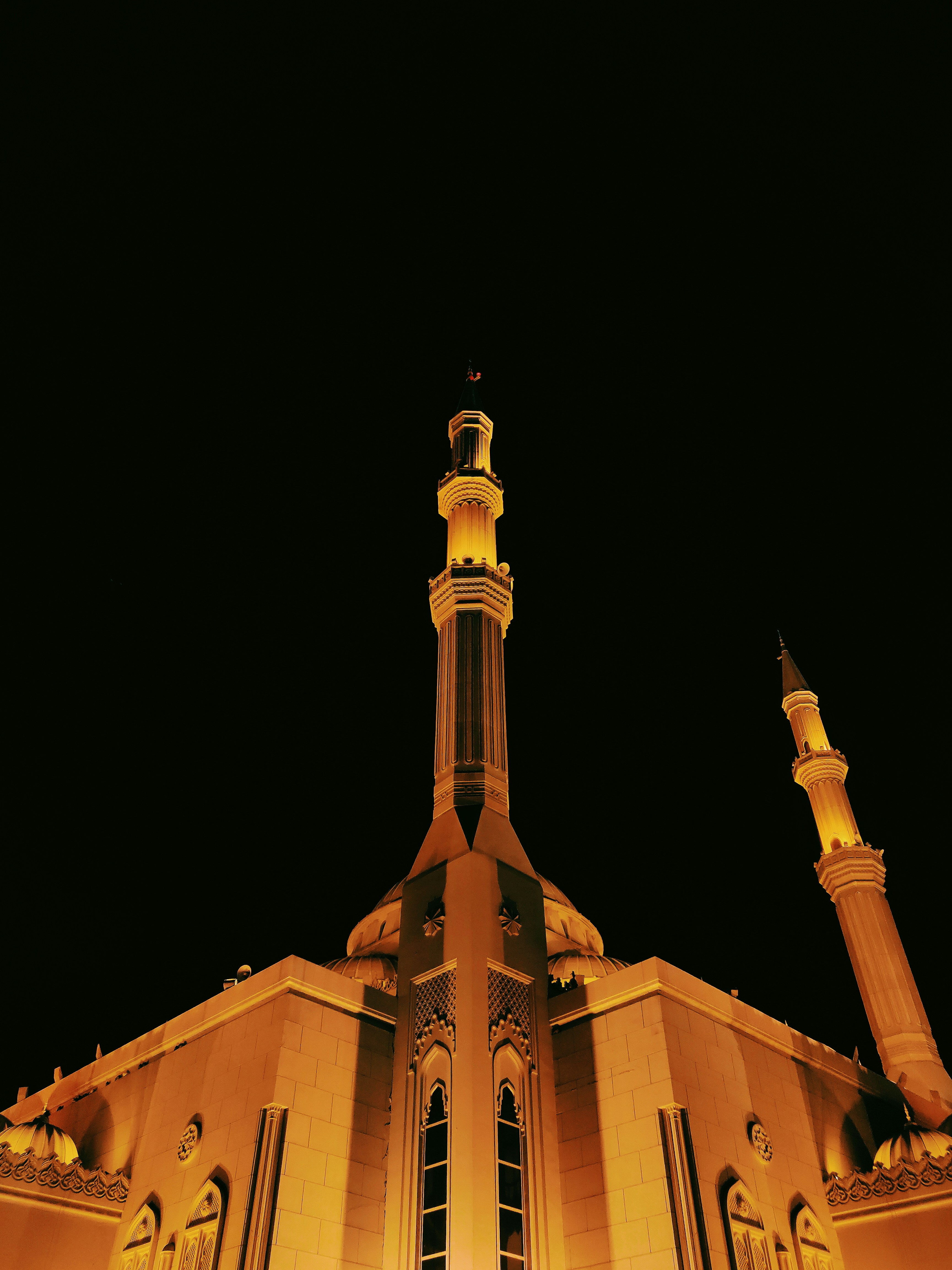 Madinah Mosque illuminated at night, golden minarets against dark sky, atmospheric low-key professional photography