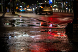An urban night scene with colorful lights reflecting on wet pavement.