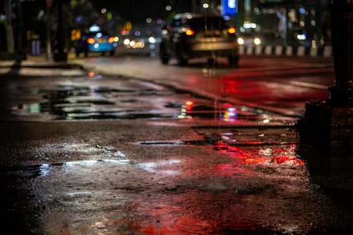 An urban night scene with colorful lights reflecting on wet pavement.
