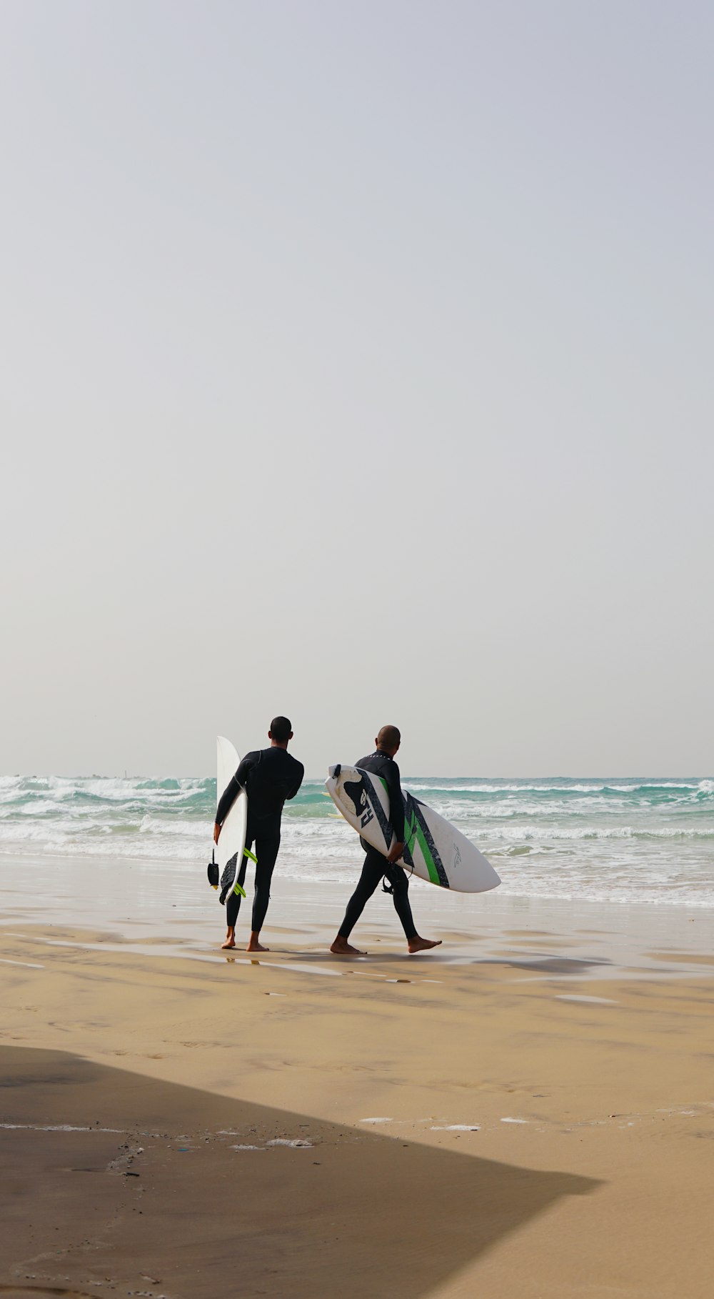 two men in wetsuit holding surfboards