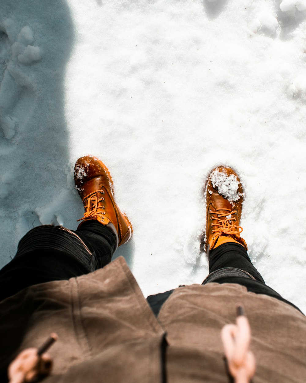 pessoa vestindo par de botas de trabalho de couro marrom em pé na neve