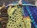 Various intertwined fishing nets with vibrant colors, including green, blue, and yellow ropes, are shown in a close-up. The image also features some rusted metal elements, such as chains and weights. The nets appear to be on a quay or dock, with a rough stone wall in the background.