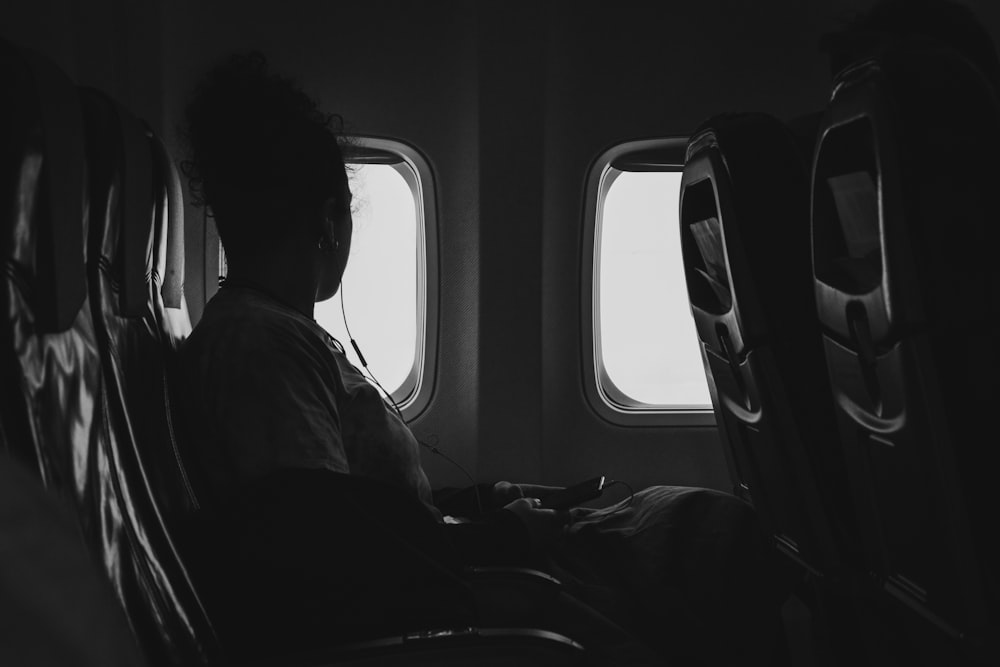 Fotografía en escala de grises de una persona que viaja en avión mientras mira la ventana