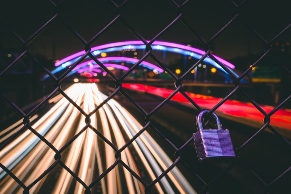 black key padlock on chain-link fence near road with cars running in time lapse photography