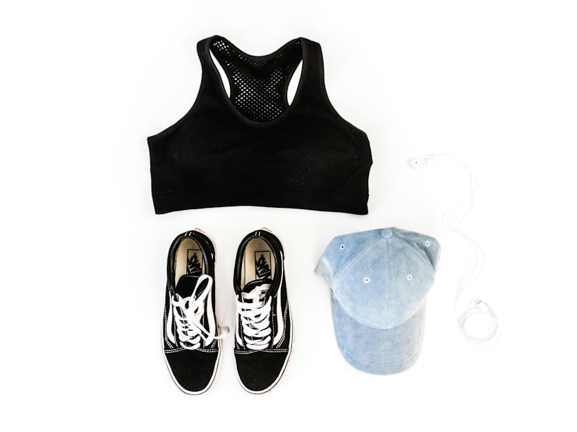 Flat lay of a black sports bra, black sneakers, and a cap on a white background