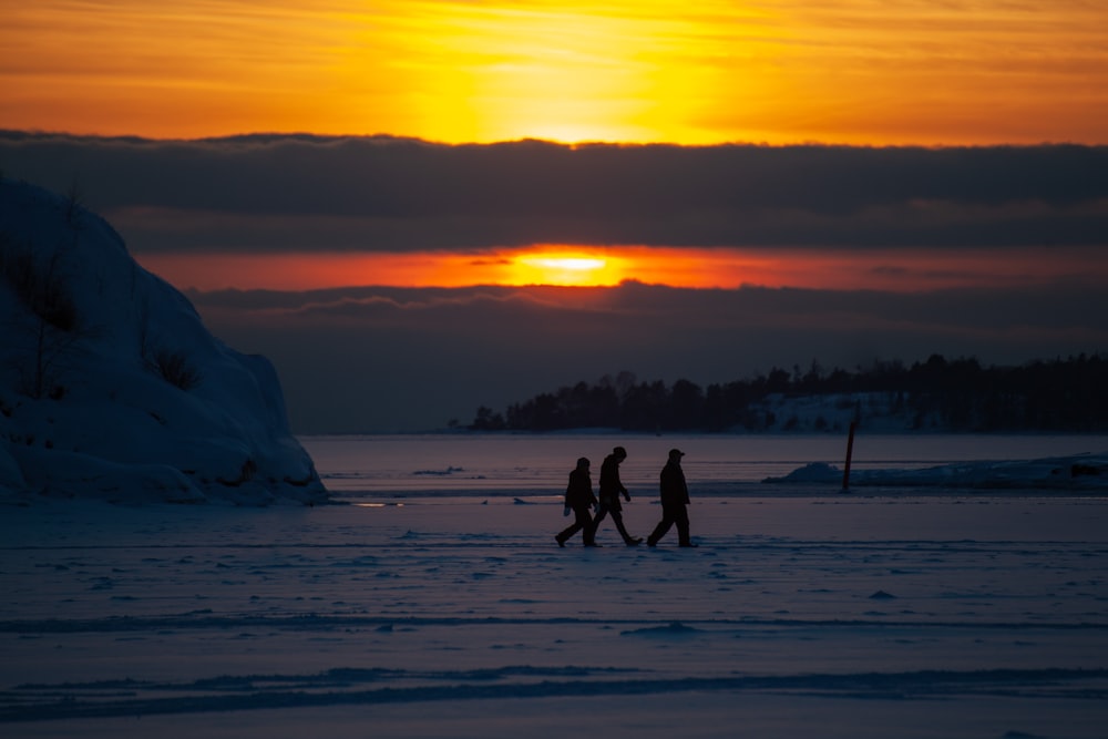 three person walking on snow during golden hour
