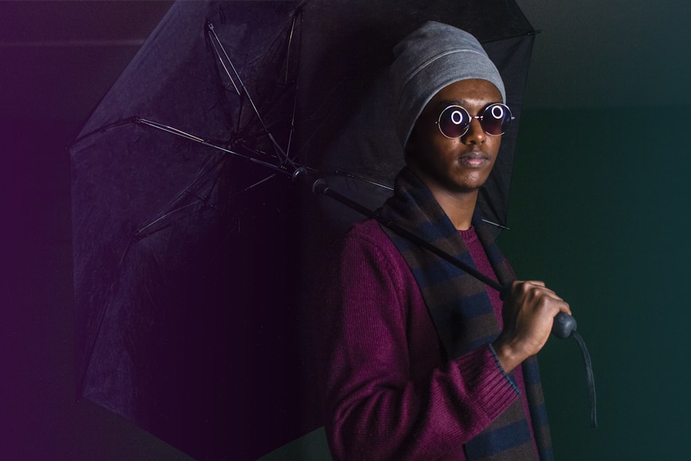 person wearing sweater, beanie, and scarf holding umbrella inside dark room