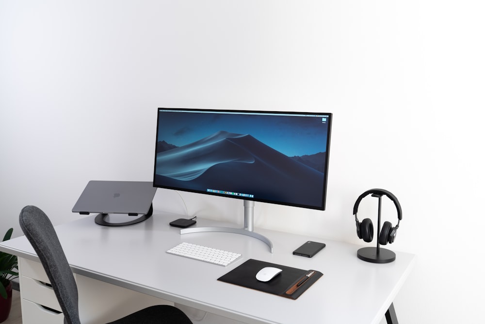 책상 위에 Apple Magic Keyboard와 마우스가 있는 검은색 평면 와이드스크린 컴퓨터 모니터
