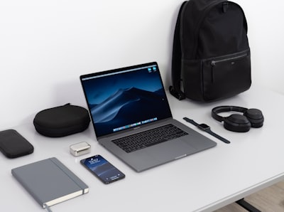MacBook Pro on table near black smartphone, cordless headphones and backpack