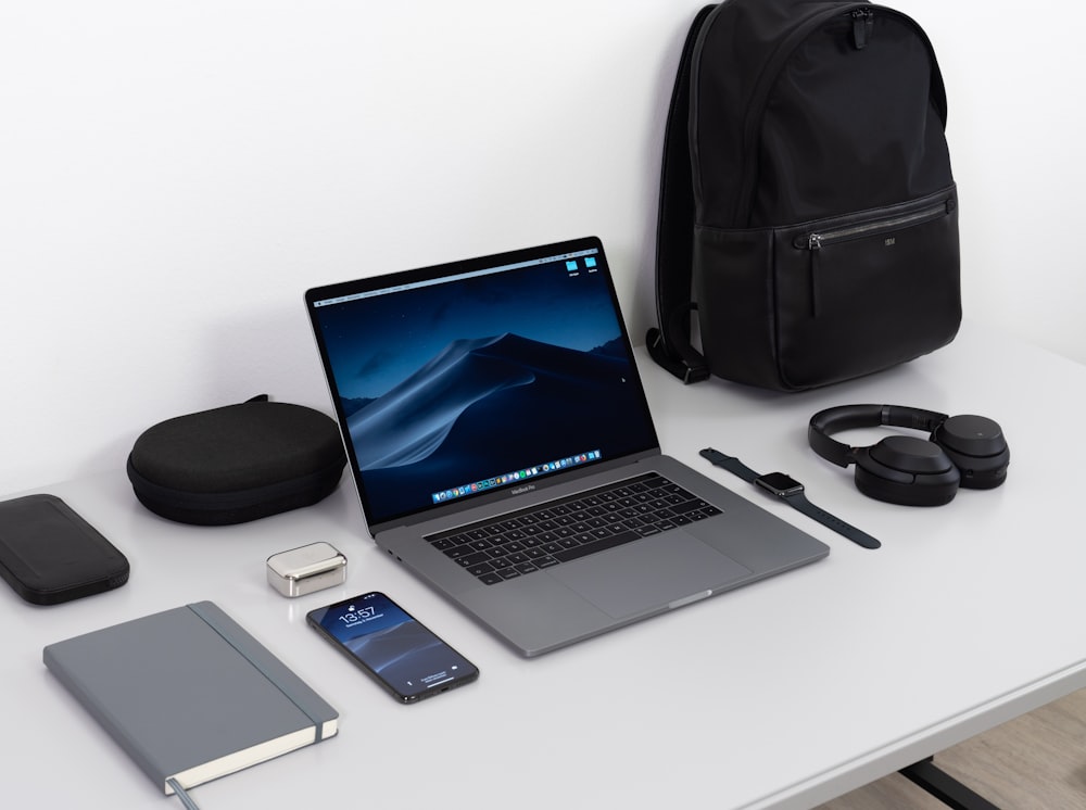 MacBook Pro na mesa perto de smartphone preto, fones de ouvido sem fio e mochila