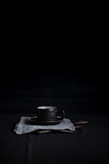 black mug and saucer on top of white textile