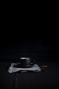 black mug and saucer on top of white textile