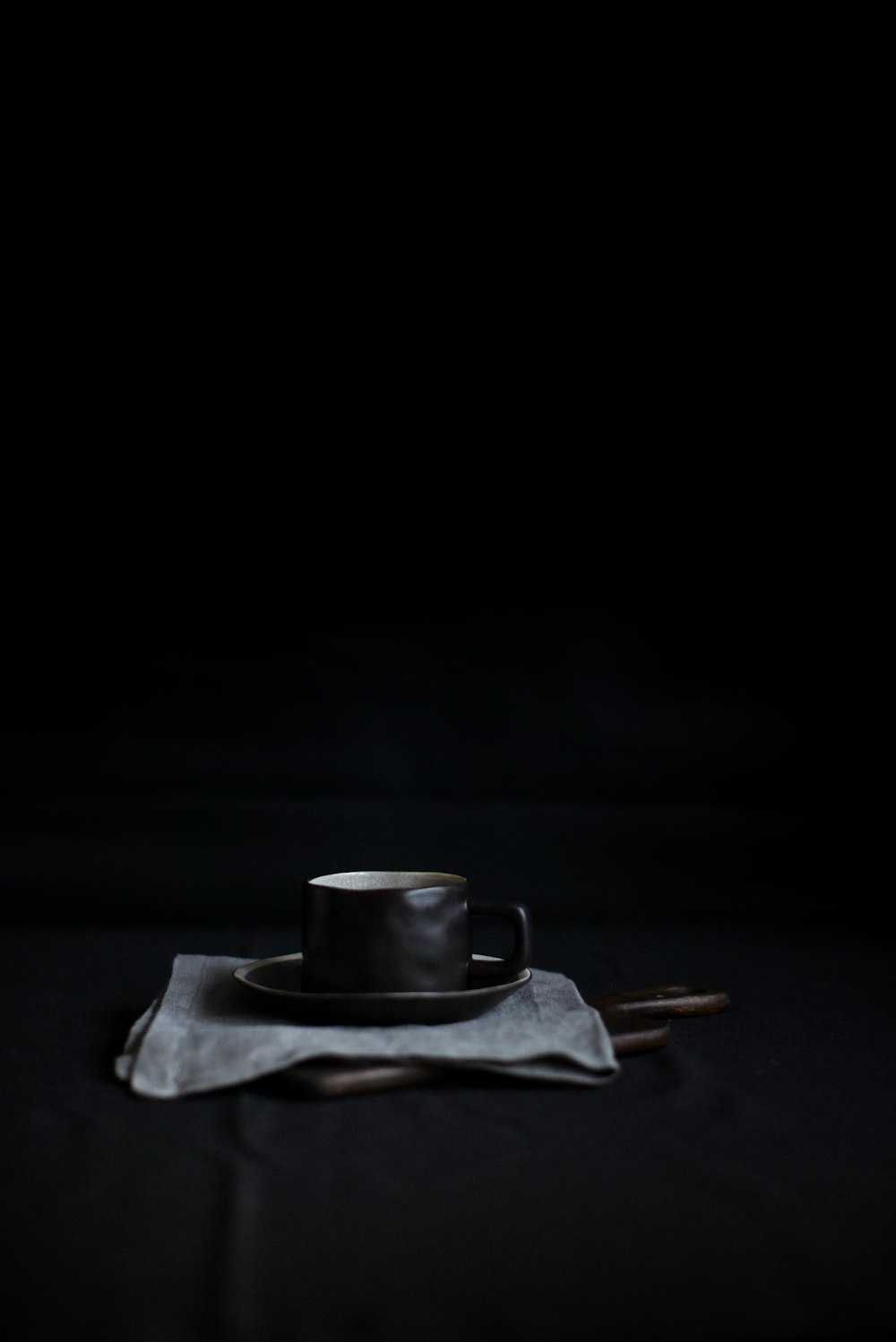 black mug and saucer on top of white textile
