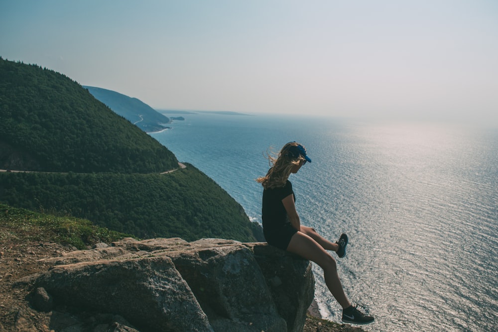 woman sitting on rock watching body of water