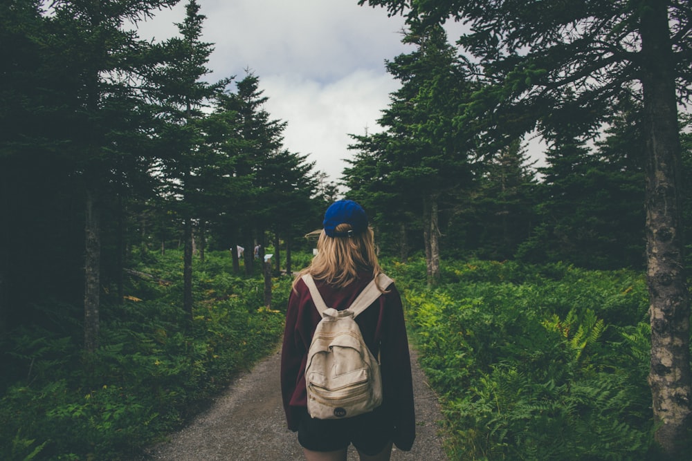 woman wearing blue cap standing on dirt road between trees during daytime