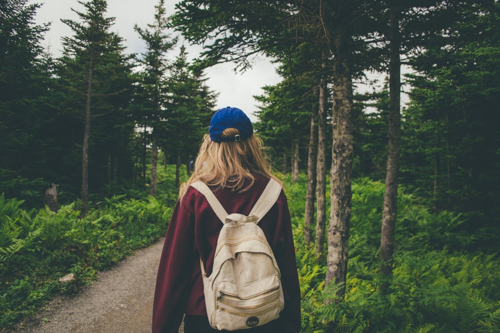 woman wearing red jacket with white backpack walking in middle of woods