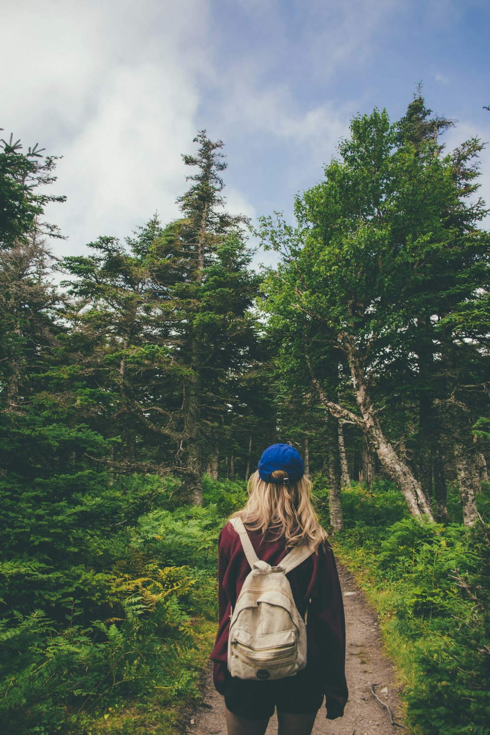 woman with backpack standing on walkway between trees and plants