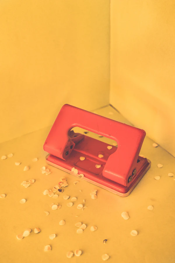 A red two-hole punch with punched paper confetti scattered around it