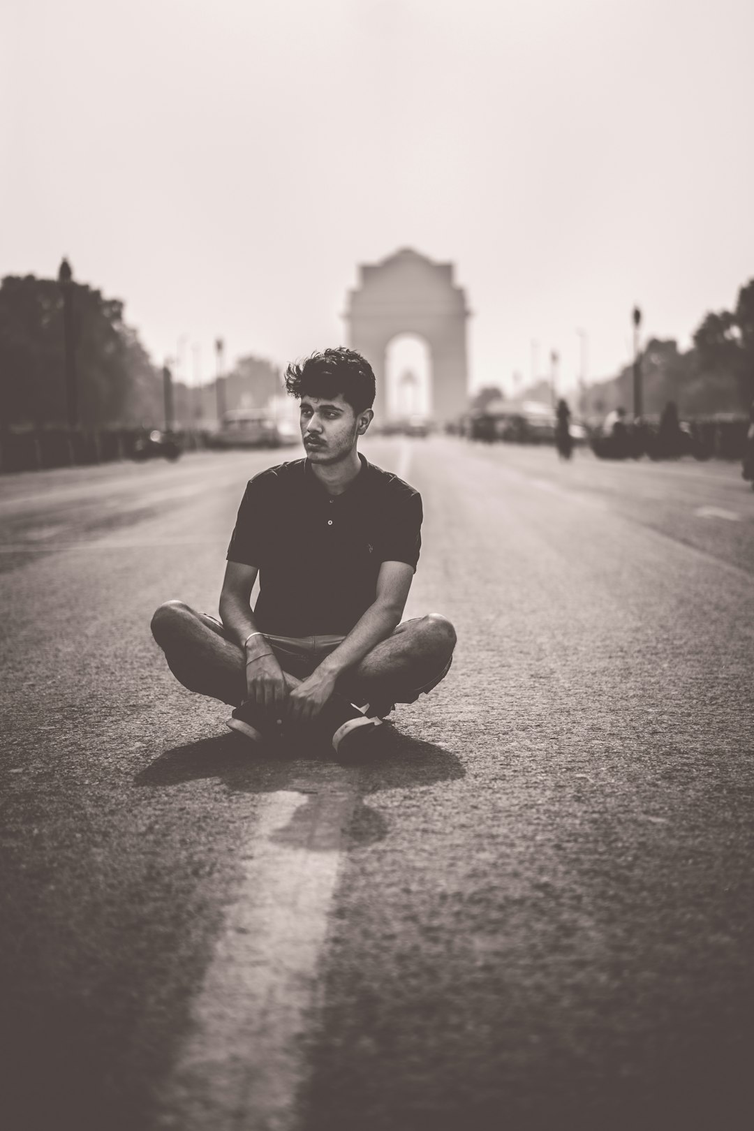 grayscale photo of man sitting on road