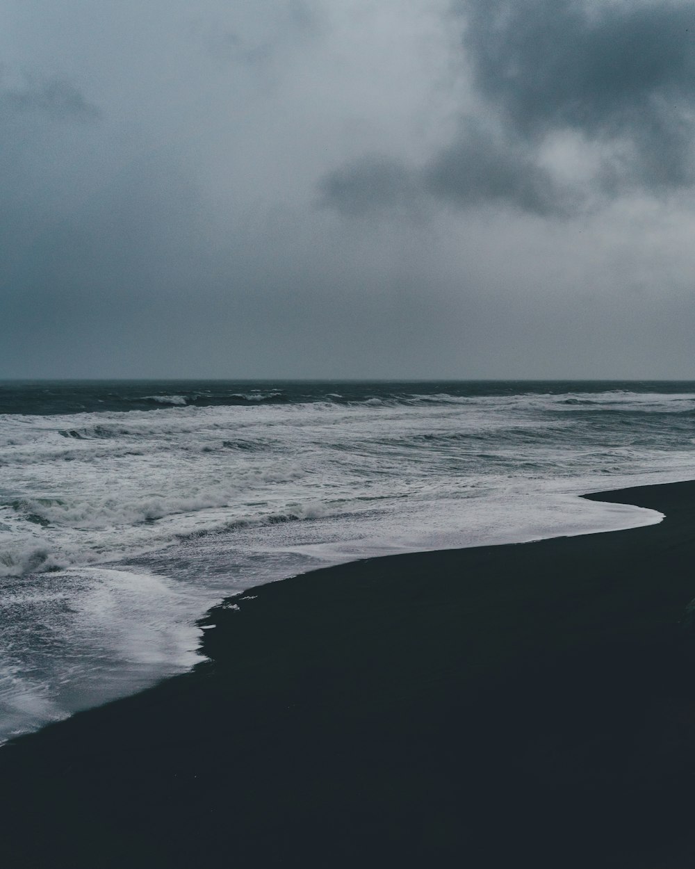 灰色の雲の下に黒い砂浜が浮かぶ海岸