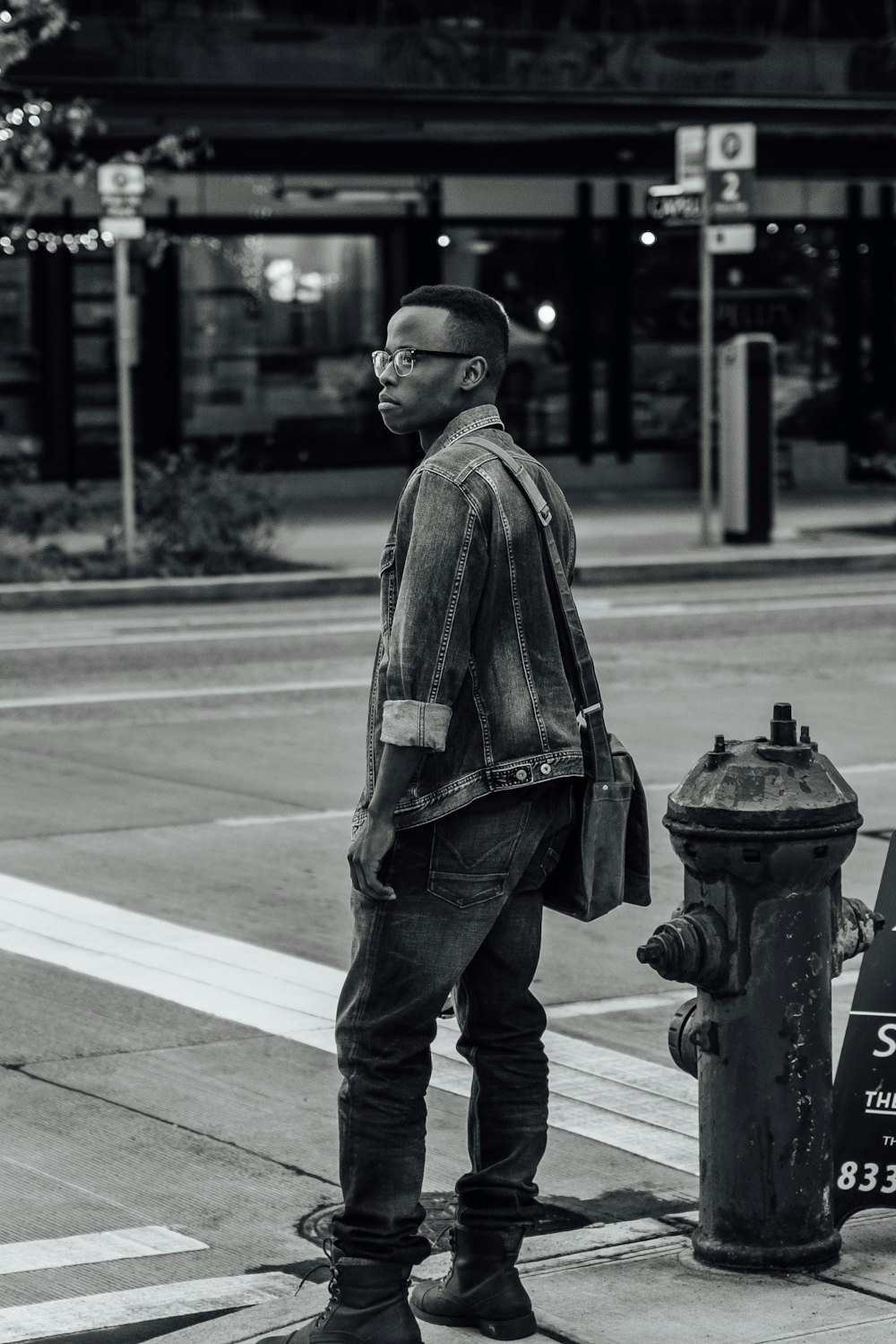 greyscale photo of man in jacket and denim jeans standing beside road