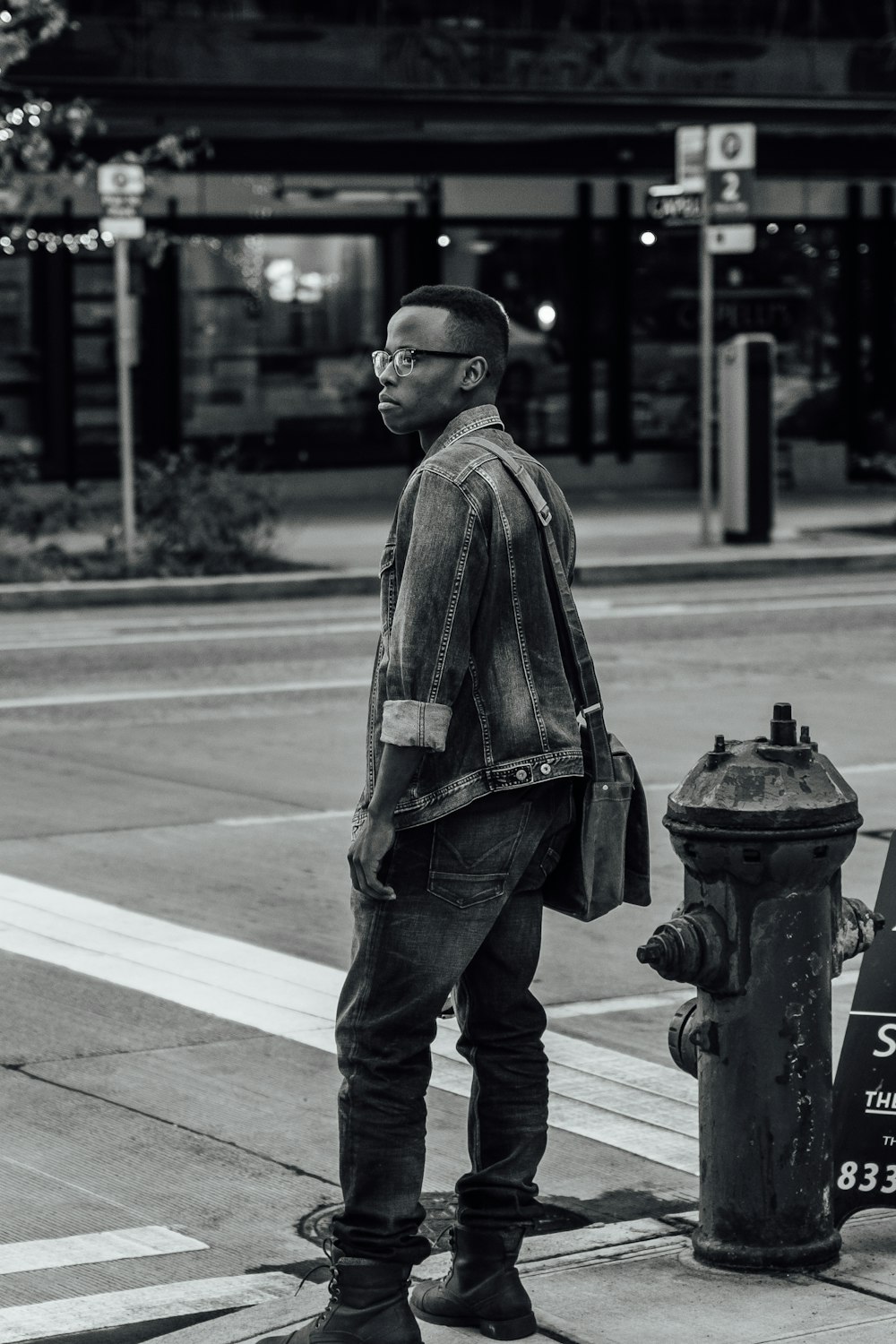 Foto in scala di grigi di un uomo in giacca e jeans di jeans in piedi accanto alla strada