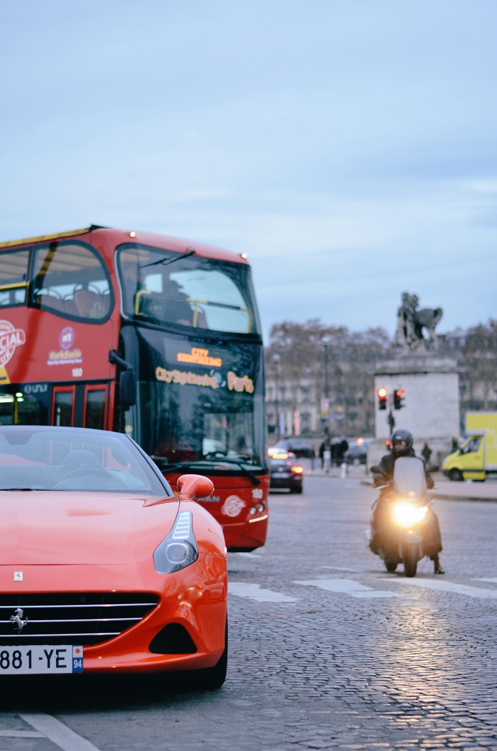 Voiture rouge à côté d’un bus près d’une statue