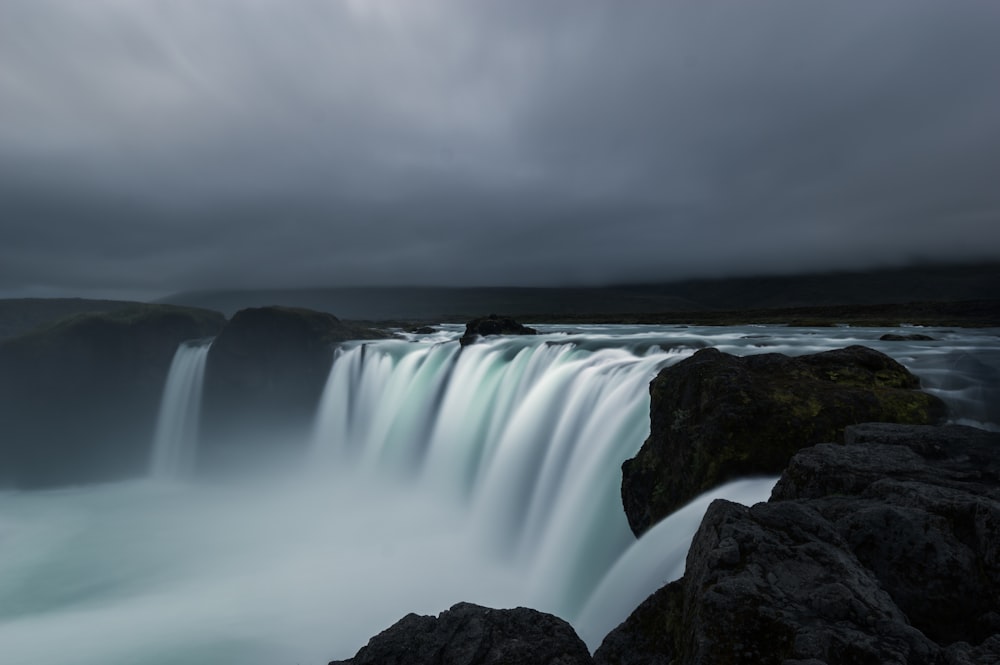 waterfalls beside black rocks under gloomy sky