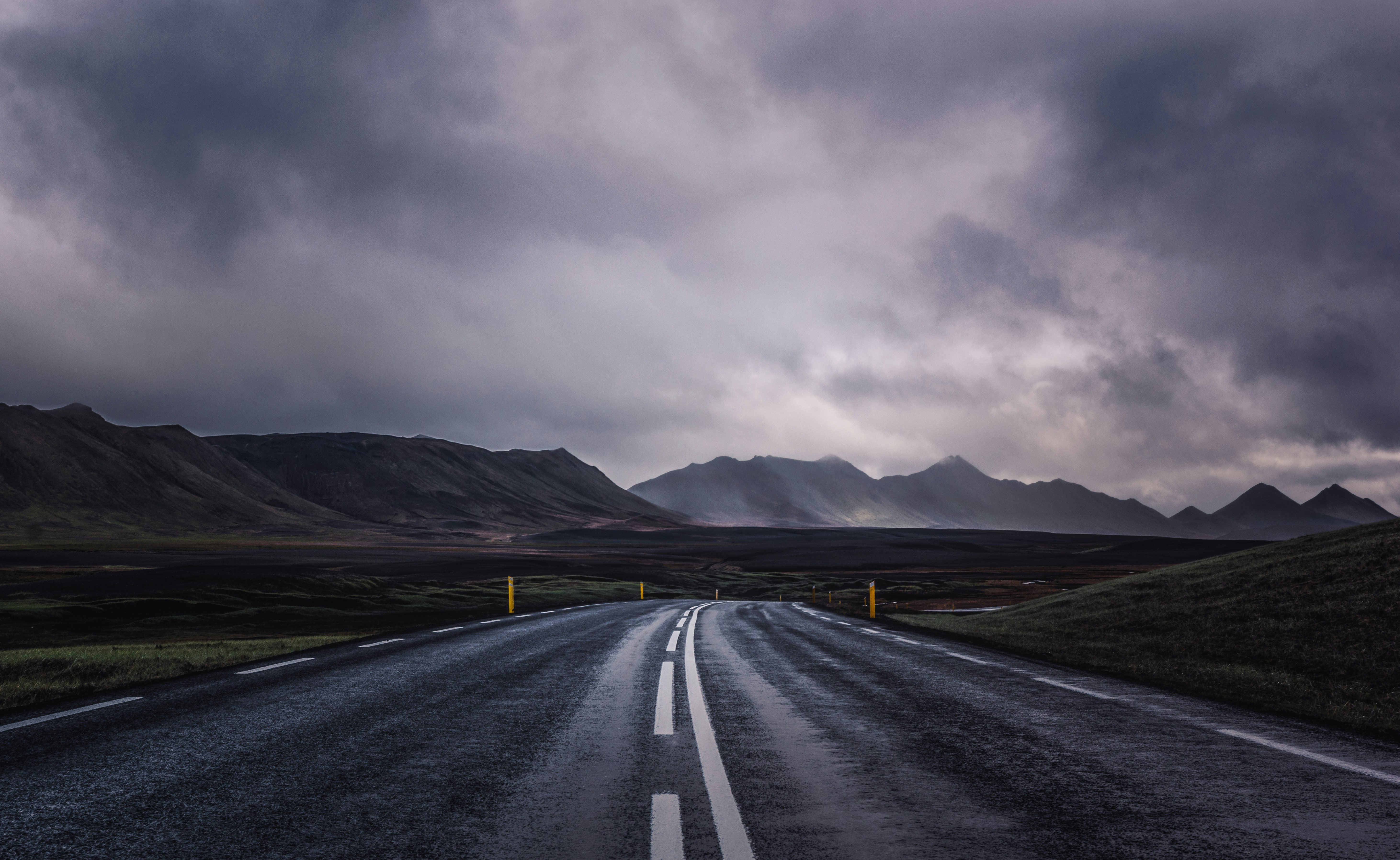 A rain-soaked road disappears into the mountains while storm clouds pass overhead.