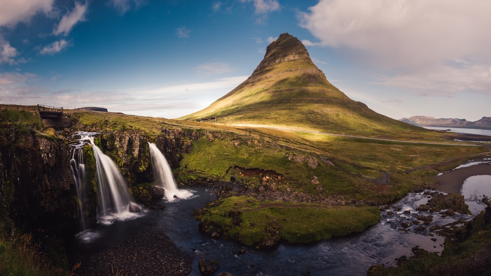 waterfalls with view of high mountain under blue sky and white clouds during daytime